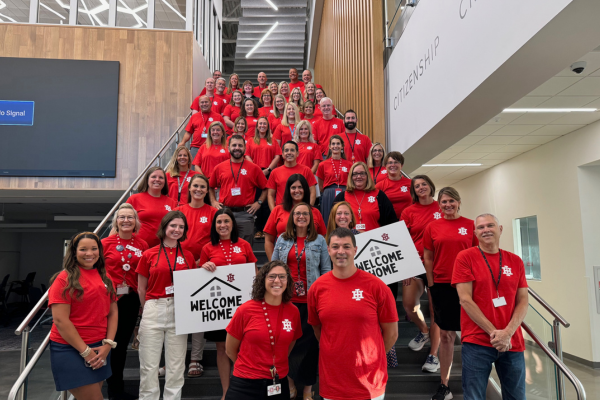 Group photo of staff inside a school building, smiling, wearing red shirts