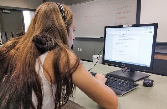 A view of the back of student with headphones on working on a desktop computer