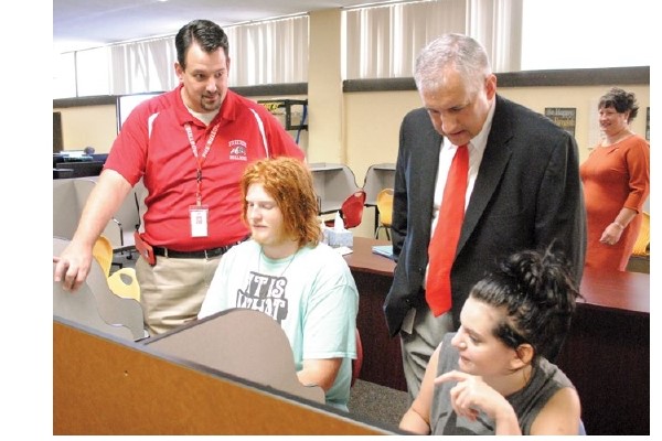 Two educators work with two students who are working independently at computer workstations