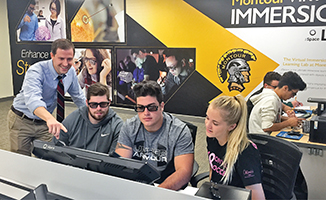 Three students work on a technical project with a teacher overlooking