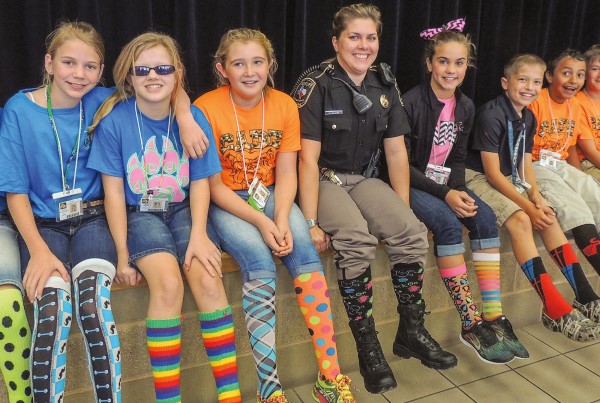 Students sit on the edge of stage in fun socks with a School Resource Officer