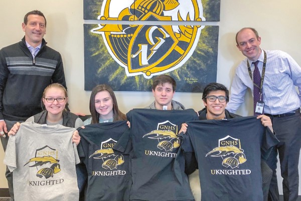 Two educators pose with four students holding up unknighted tshirts