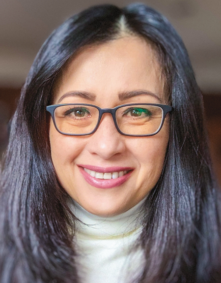 A woman with black hair and black glasses wearing a white turtleneck