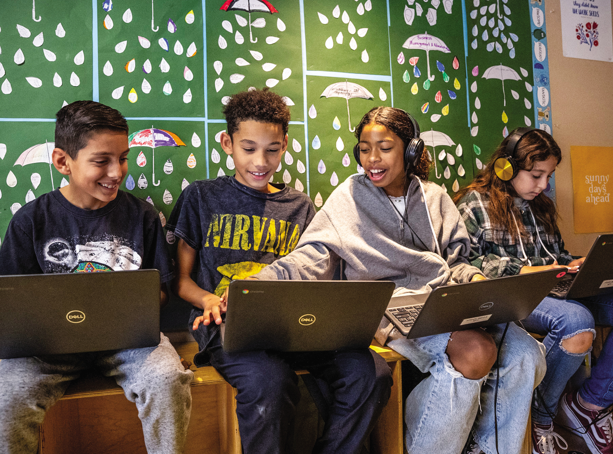 Four teens sit in a row on their computers, interacting