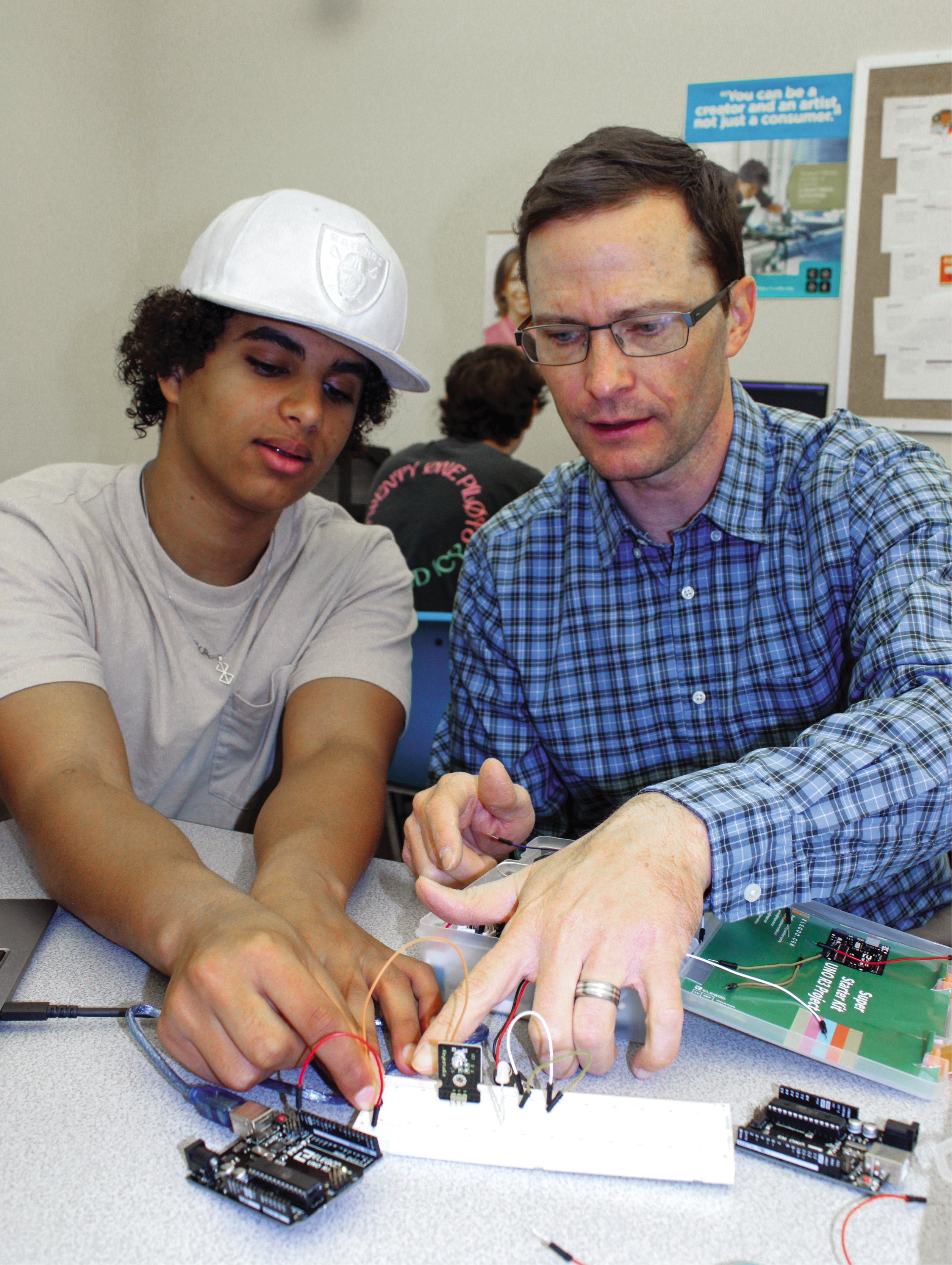 A high school student and his teacher work on building something electronic in class