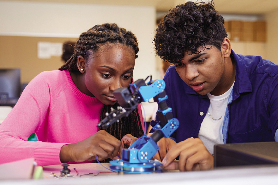 Two high school students build or look at a robotic arm