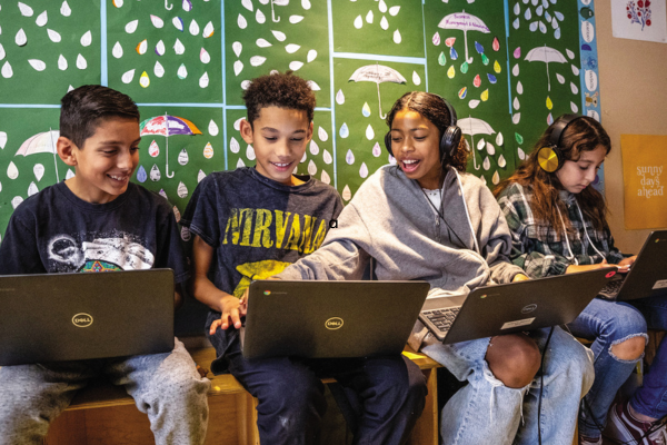 four young teens sitting and interacting together on their computers