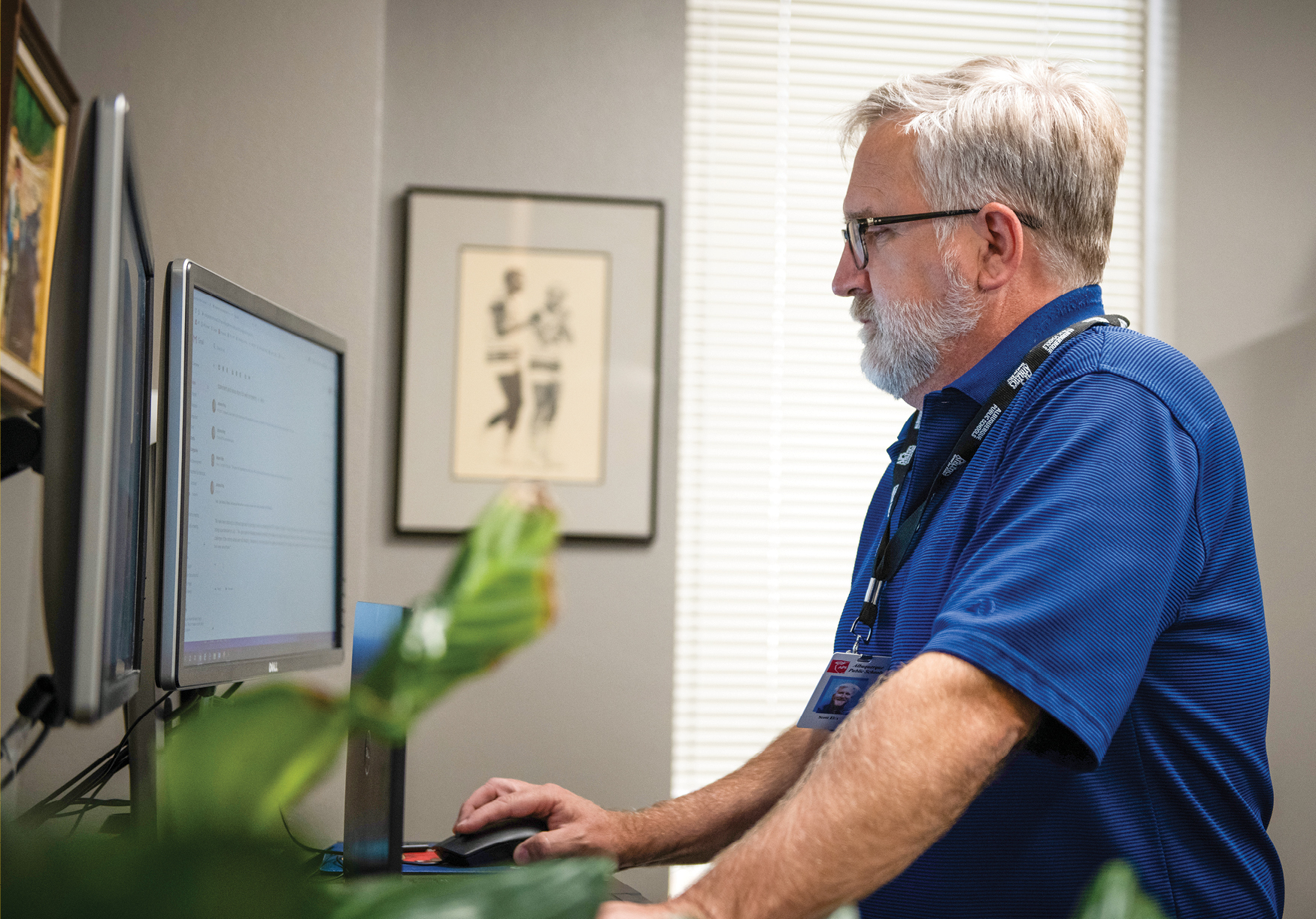 Scott Elder, a white man with gray hair and beard wearing a blue shirt and working on his computer