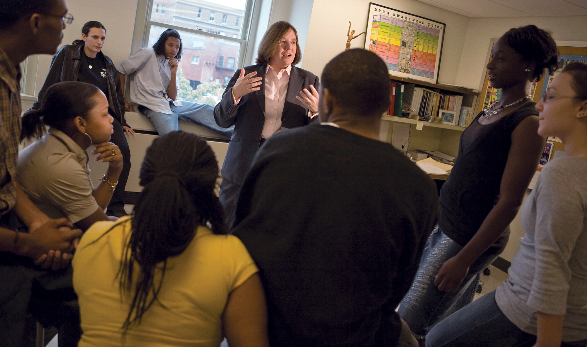 A white woman standing in the center of a group of teens talking