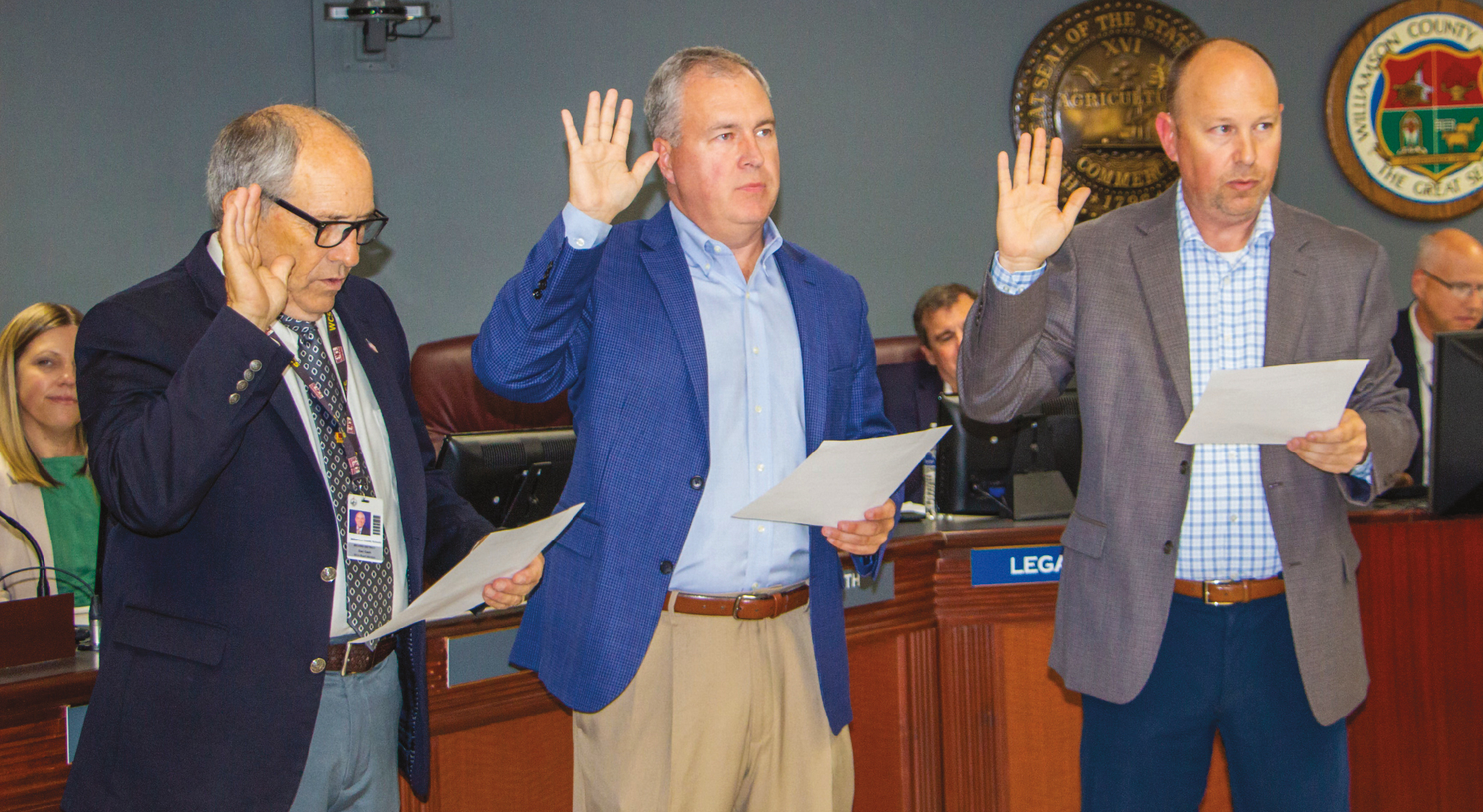 Three White men in suits standing holding a paper and raising their right hands