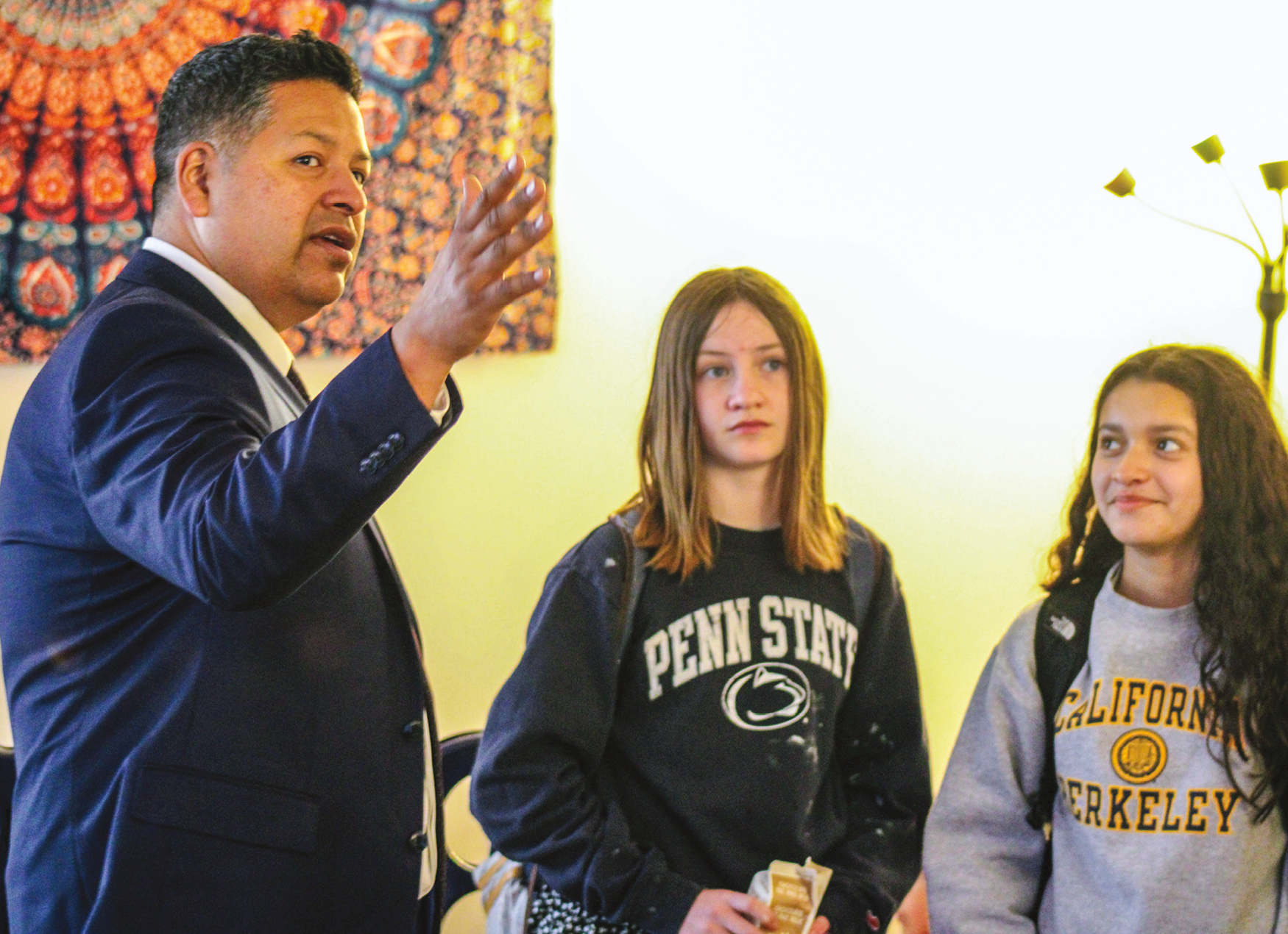 A man in a suit talking to two teenagers in college sweaters