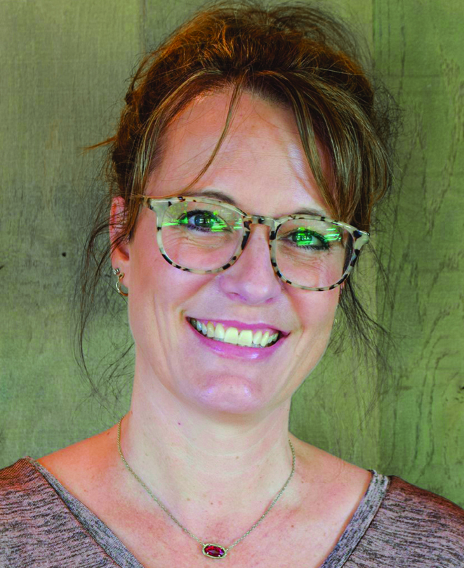 A white woman with light brown hair in an up-do smiling, wearing glasses