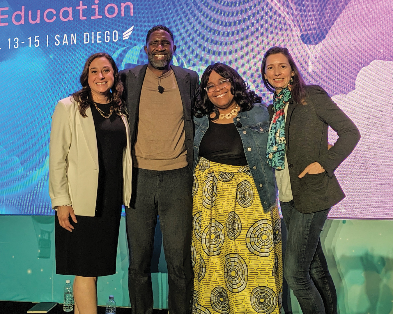 Four people, including Pati Ruiz (right), on stage at an event smiling and posing