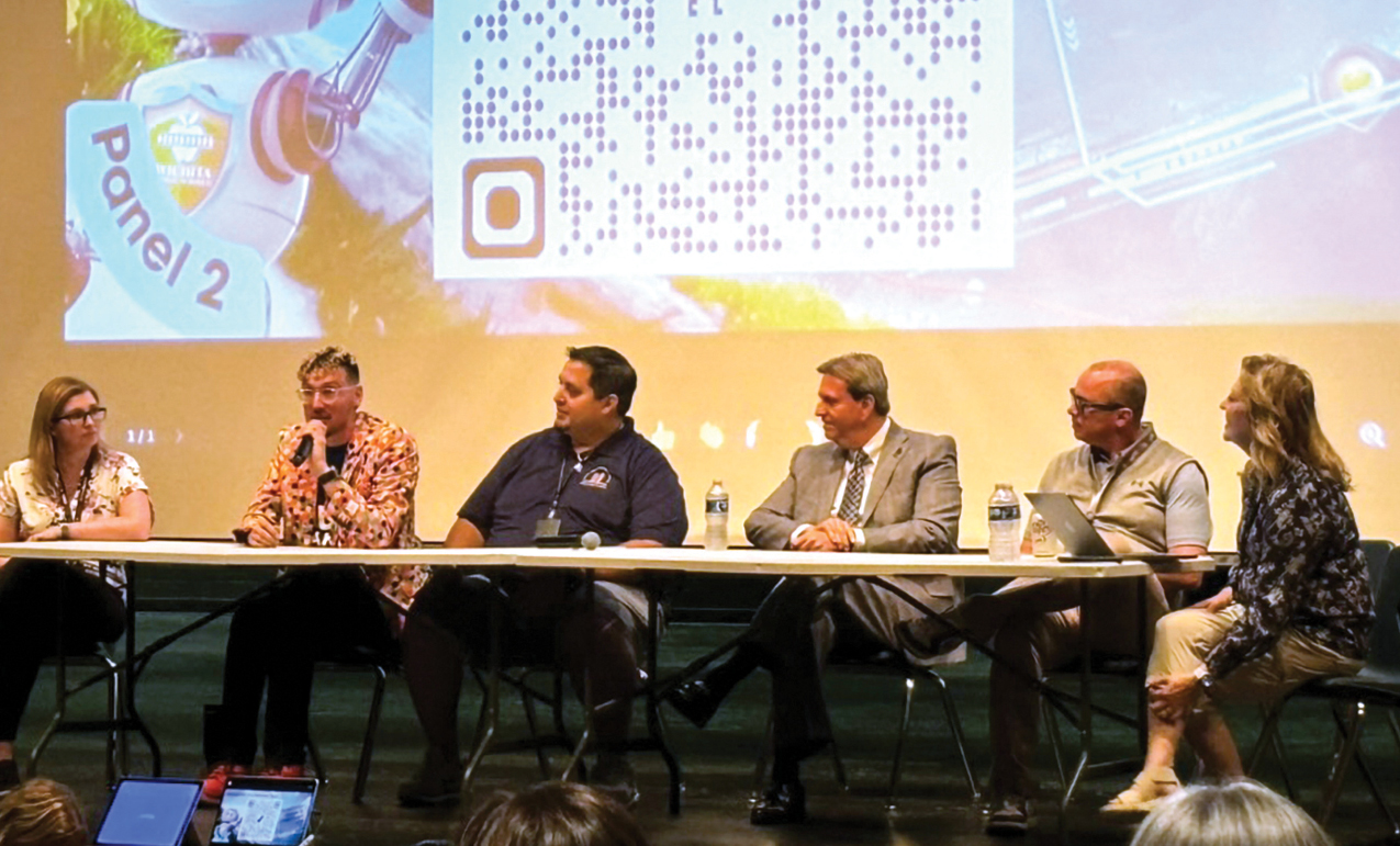 Six panelists, including Rob Dickson and Dyane Smokorowski (right) sitting at a table in front of a presentation