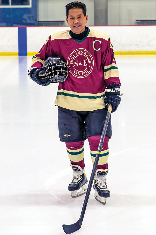 A man in a hockey uniform holding his stick and helmet while on the ice