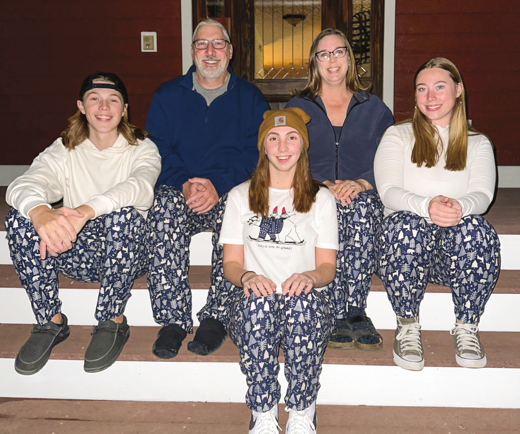 A family of five sitting on the steps, all wearing matching pajama pants