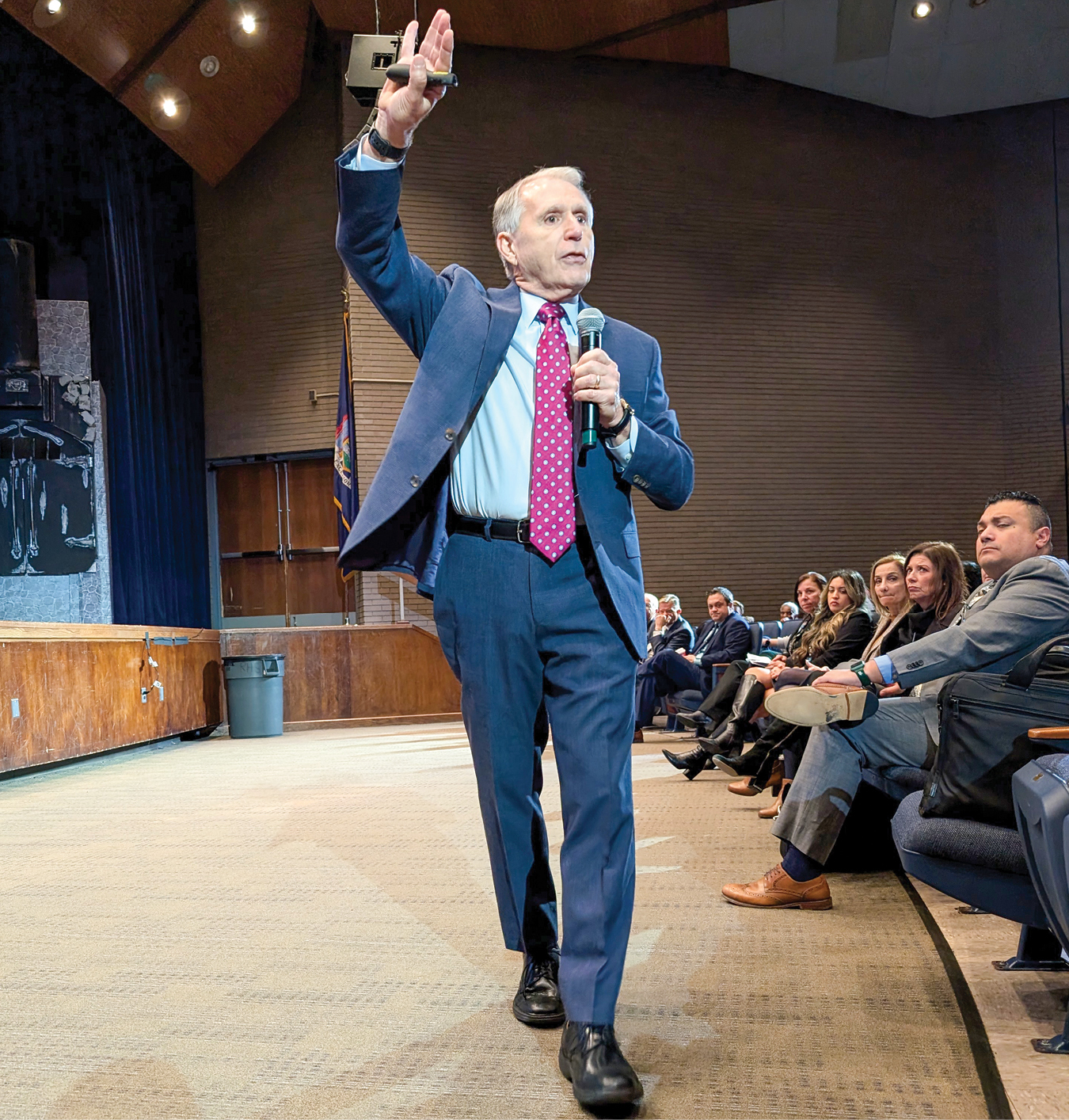 A man speaks to a crowd with a microphone while gesturing