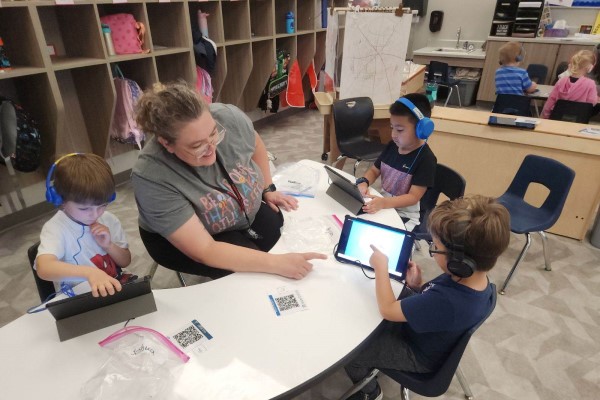 Preschoolers work on computers with assistance from a teacher